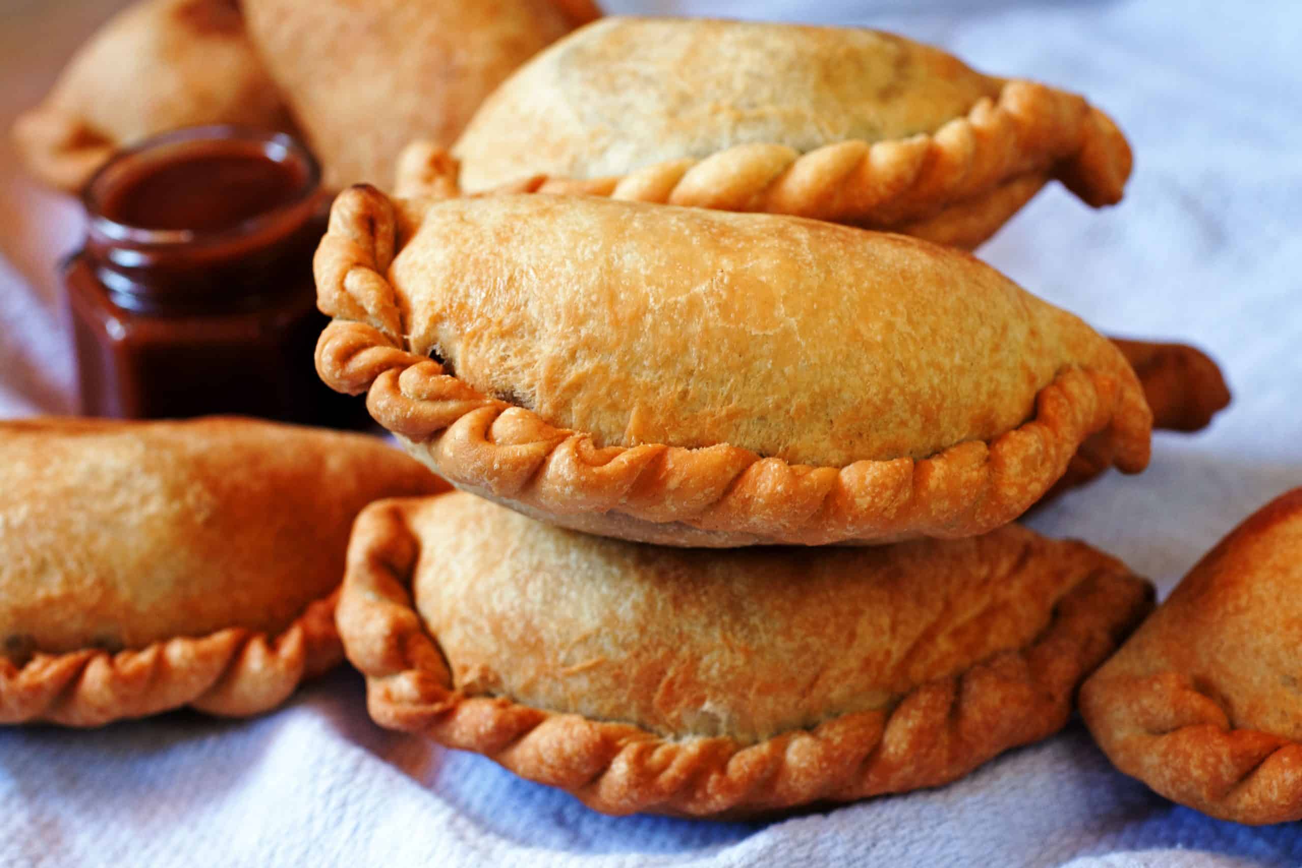 Bolivian chicken empanada with a golden crust, broken open to reveal chicken with onion, egg and ají amarillo.